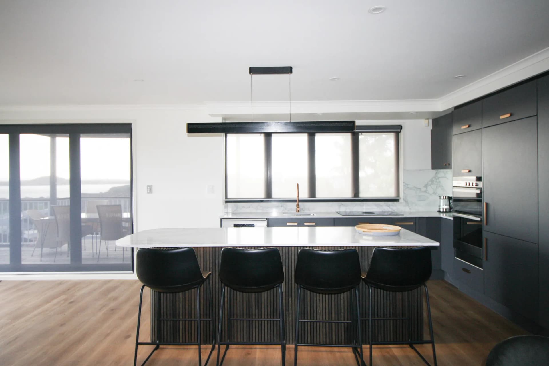 Charcoal kitchen with a fluted island and four black bar stools under a linear pendant