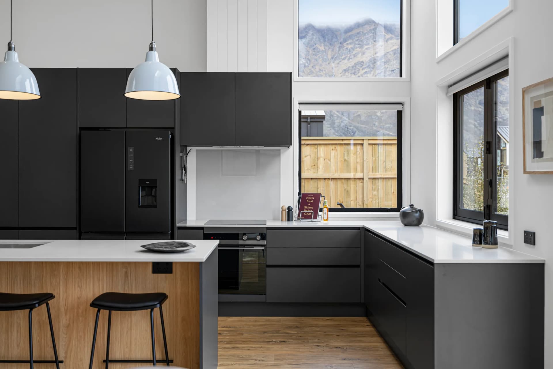 Black handleless kitchen with a timber-look island and mountain view through the window