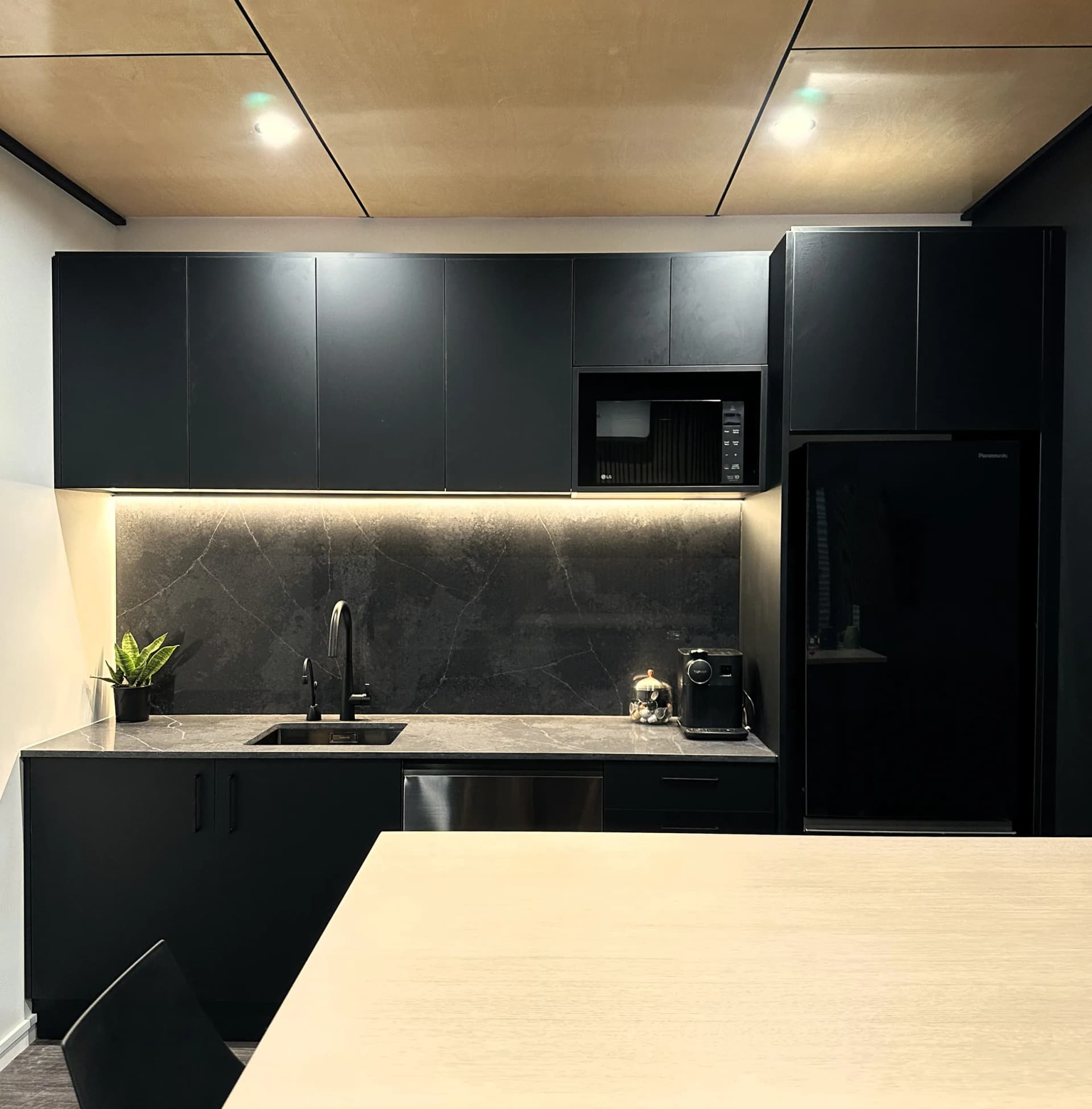 Black kitchenette with LED strip lighting above a stone-look splashback