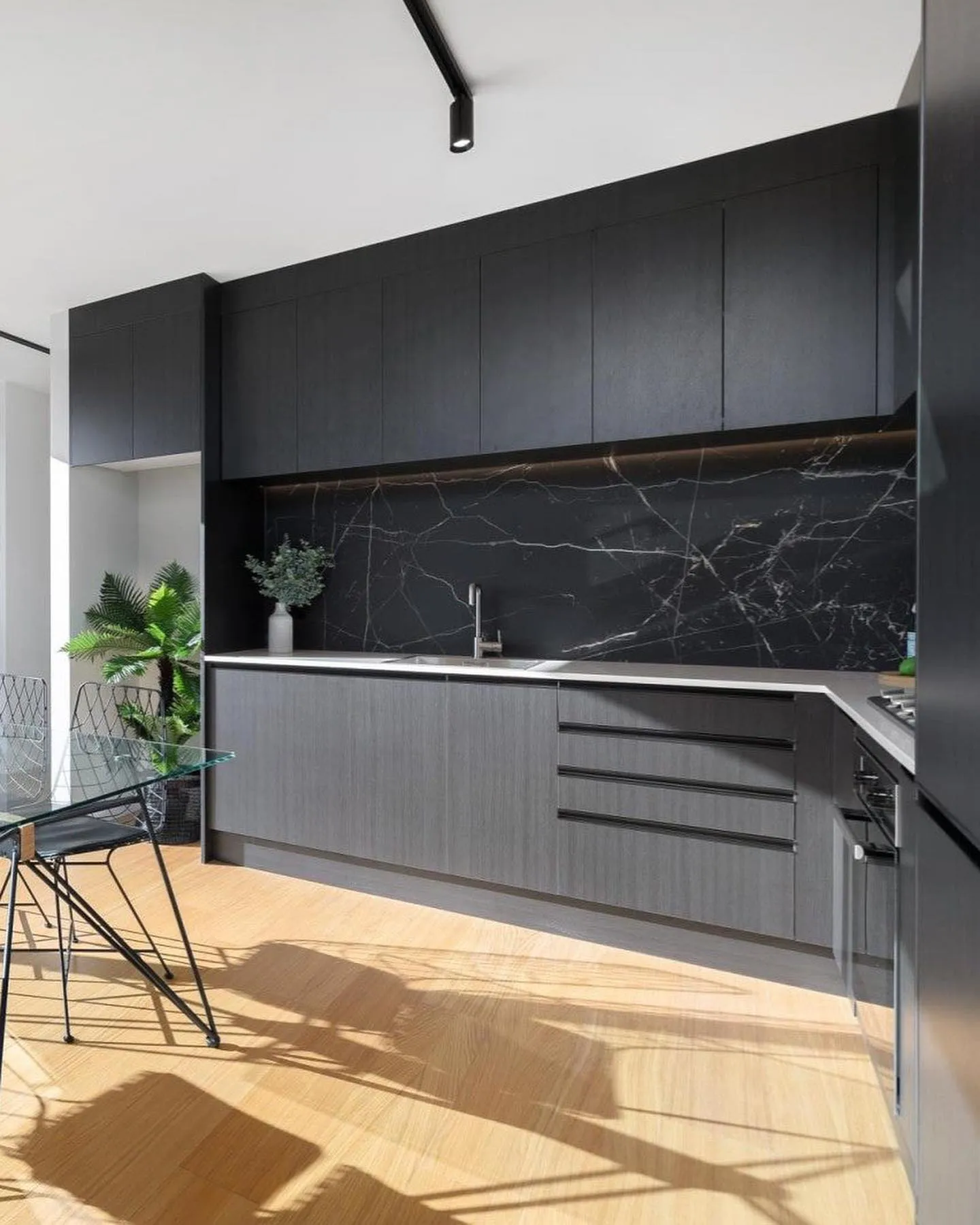 Black L-shaped kitchen with bar handles and a stone-look splashback