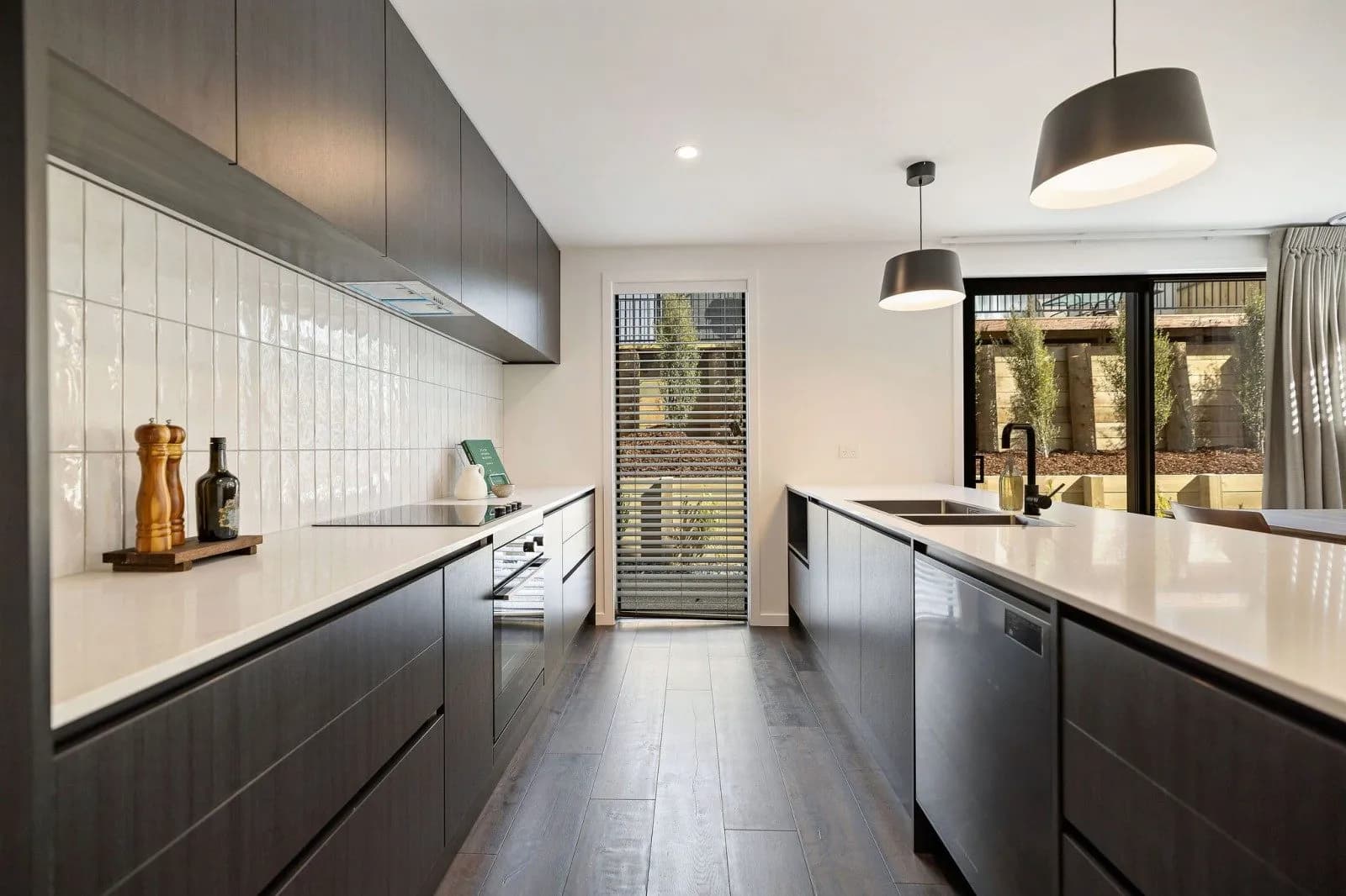 Dark timber-look galley with a white tiled splashback and black pendant lights