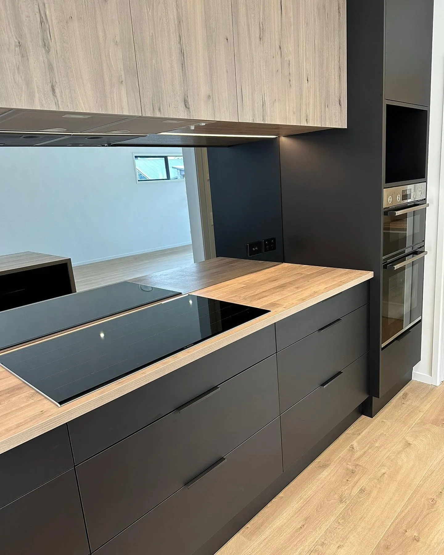 Black drawers with handles below timber-look overheads and a wall oven tower