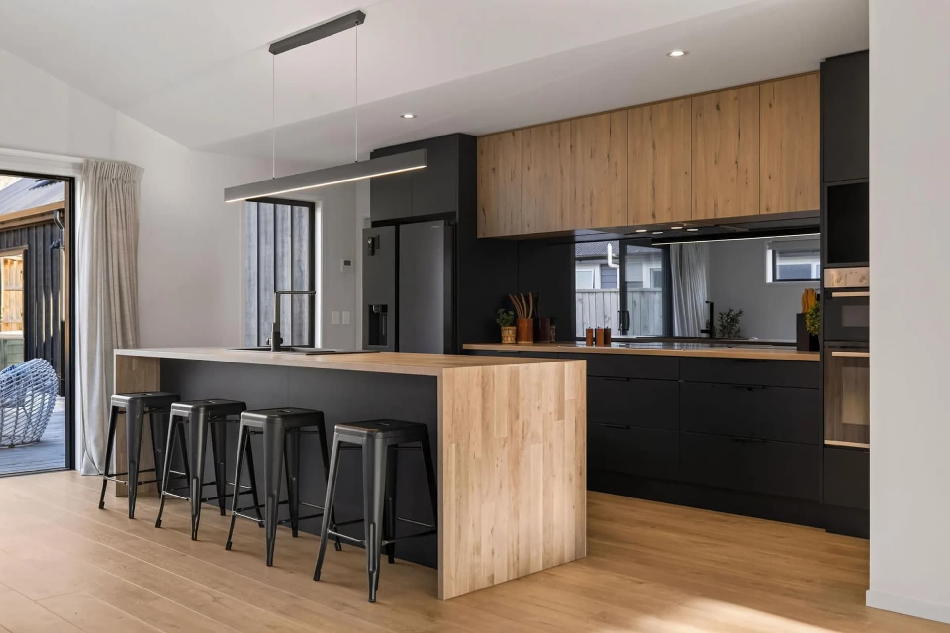 Black kitchen with a timber-look waterfall island, bar stools and timber-look overhead cabinets