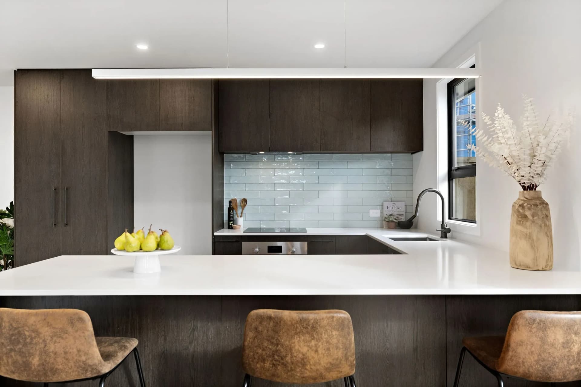 Dark timber-look U-shaped kitchen with a breakfast bar and a pale blue tiled splashback