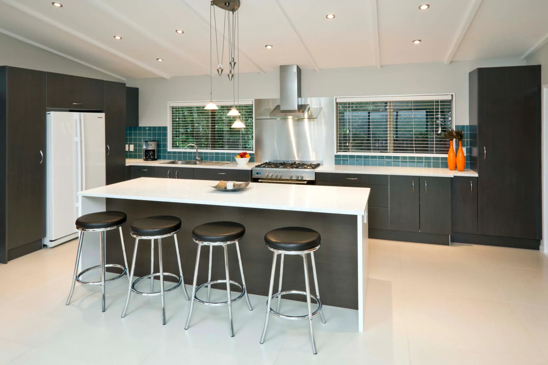 Charcoal cabinets and a white island with bar stools below a canopy rangehood