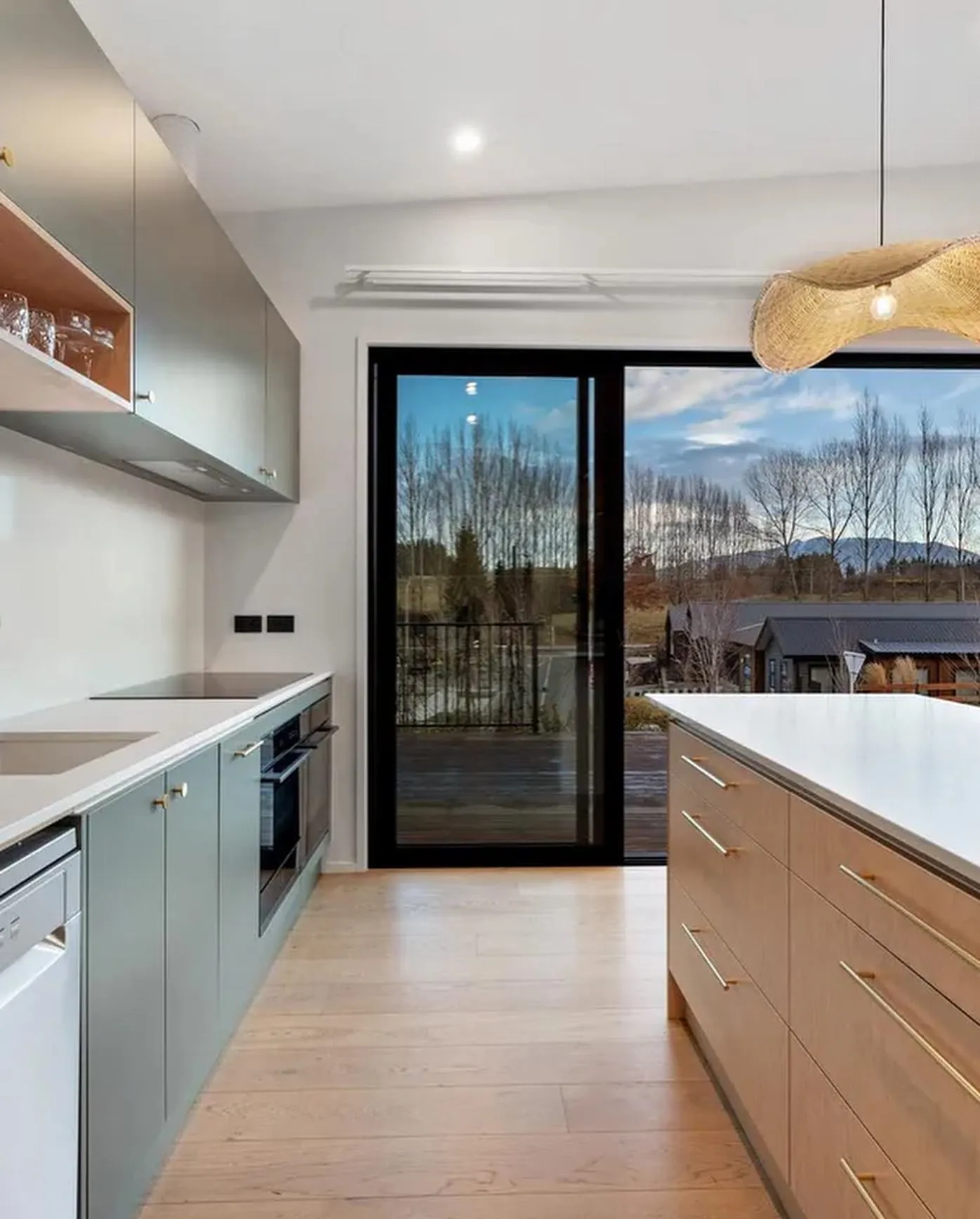 Teal cabinets and a timber-look island with gold-look handles leading to a view