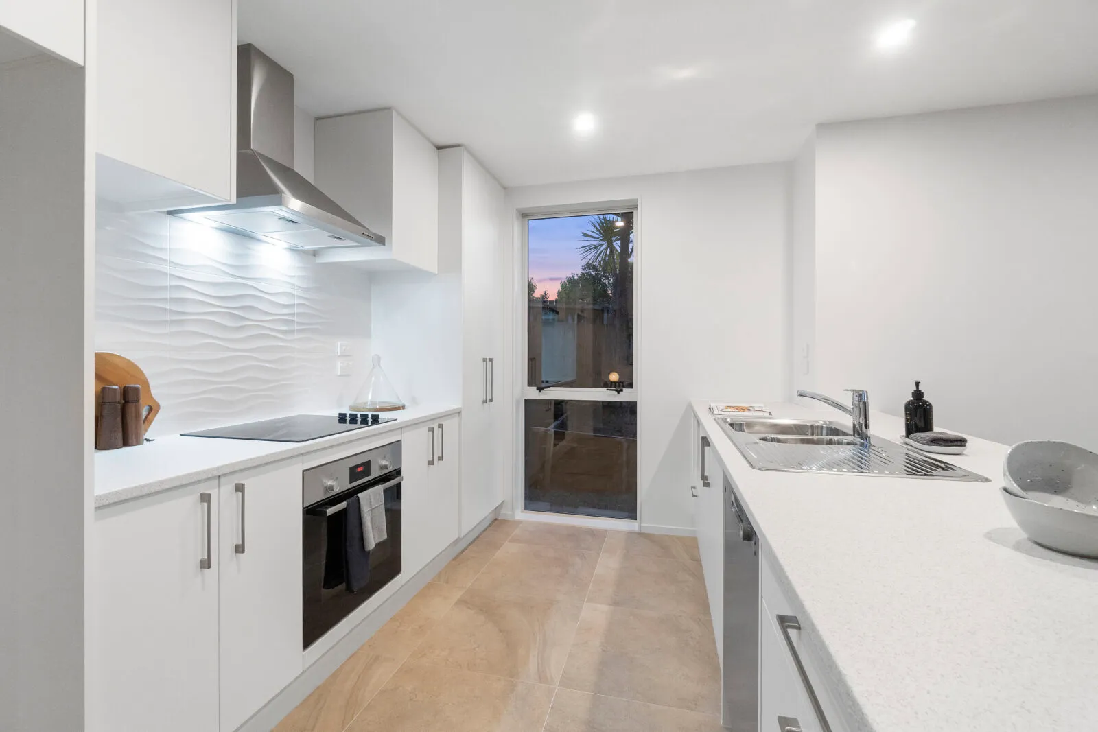 White galley kitchen with bar handles, a textured splashback and a rangehood