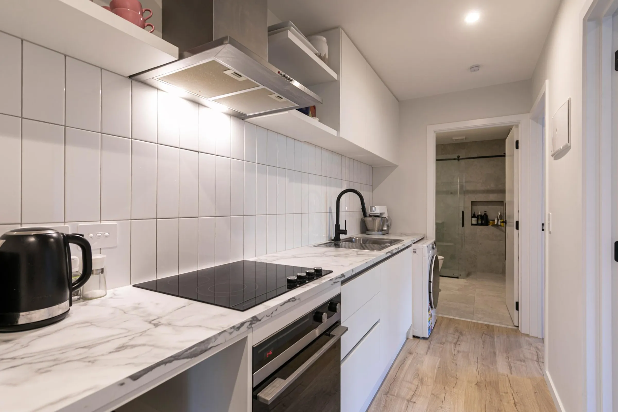 White galley kitchenette with a white tiled splashback and a rangehood