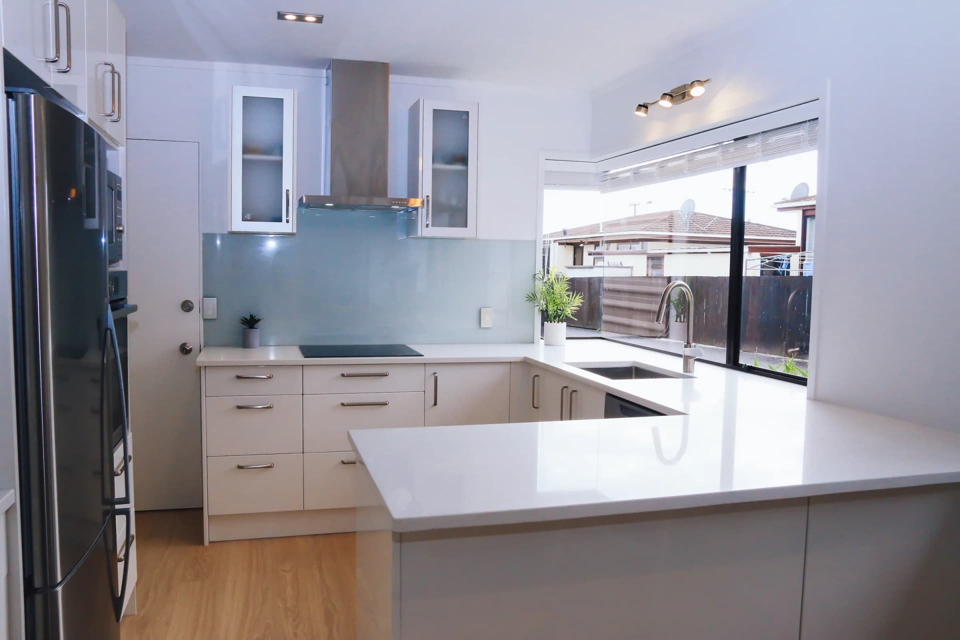 White gloss U-shaped kitchen with bar handles, a pale glass splashback and a peninsula
