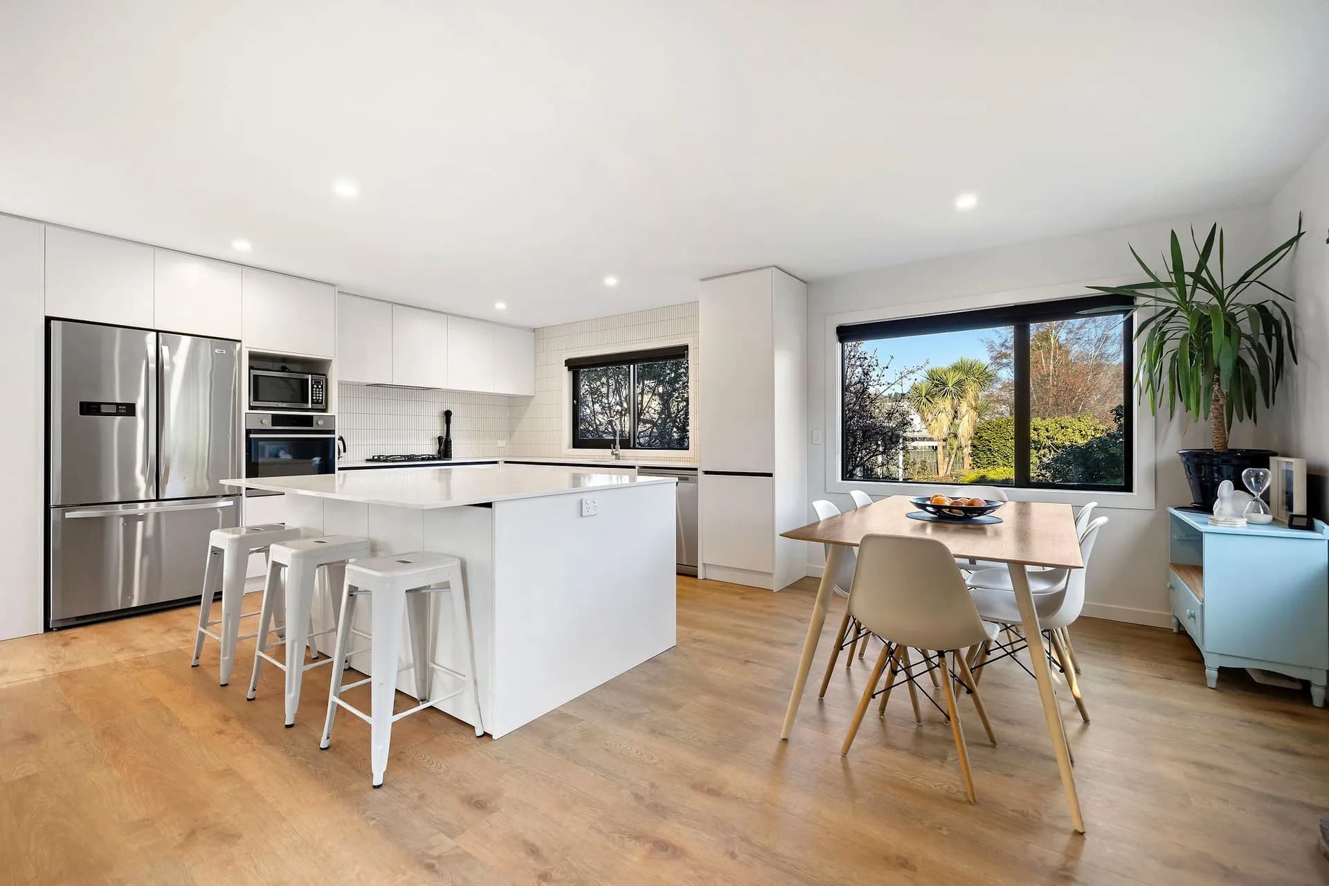 White island with stools in front of tall cabinets and a window over the sink
