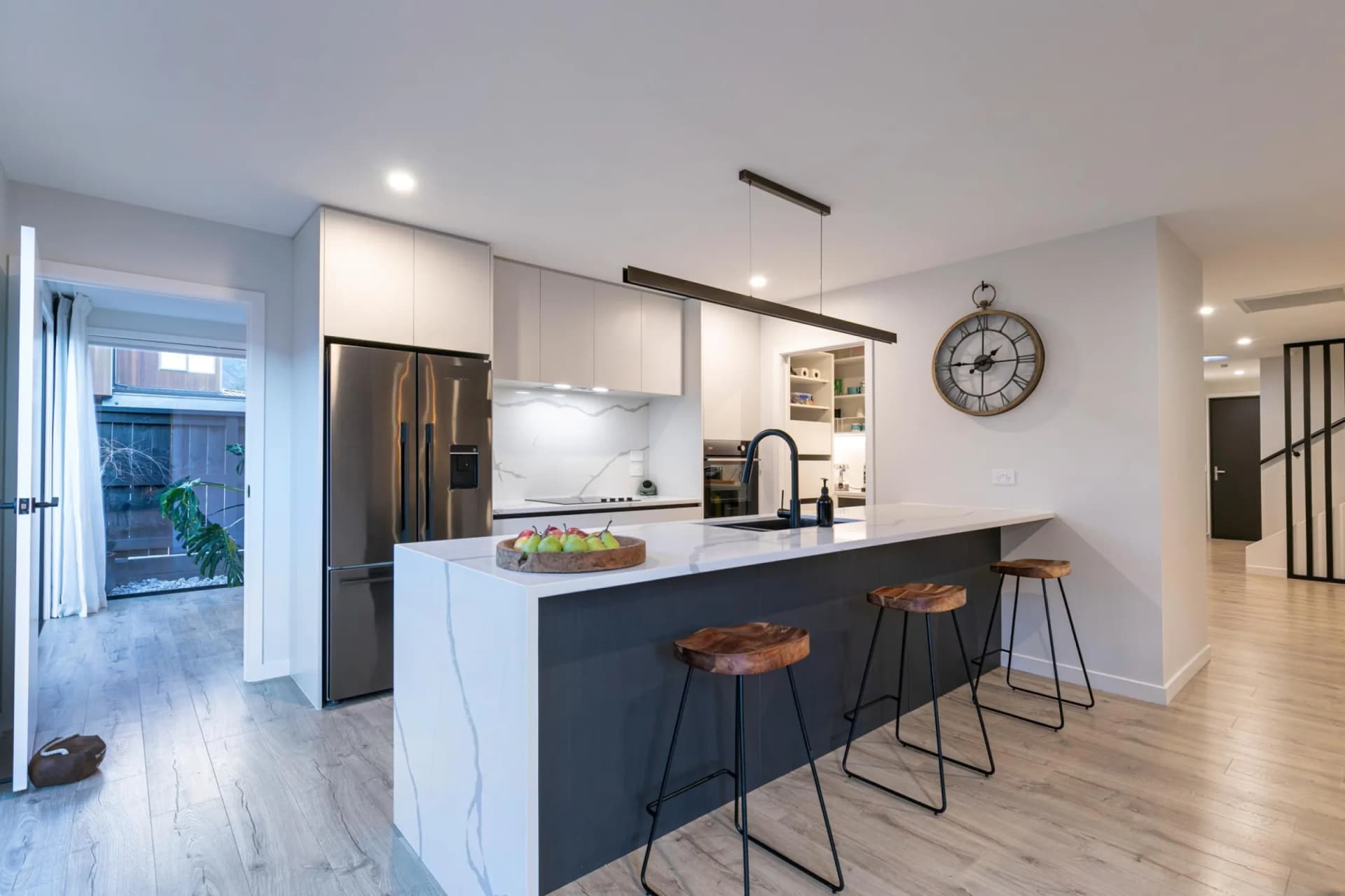 Dark island with a marble-look waterfall end and bar stools in front of white cabinetry