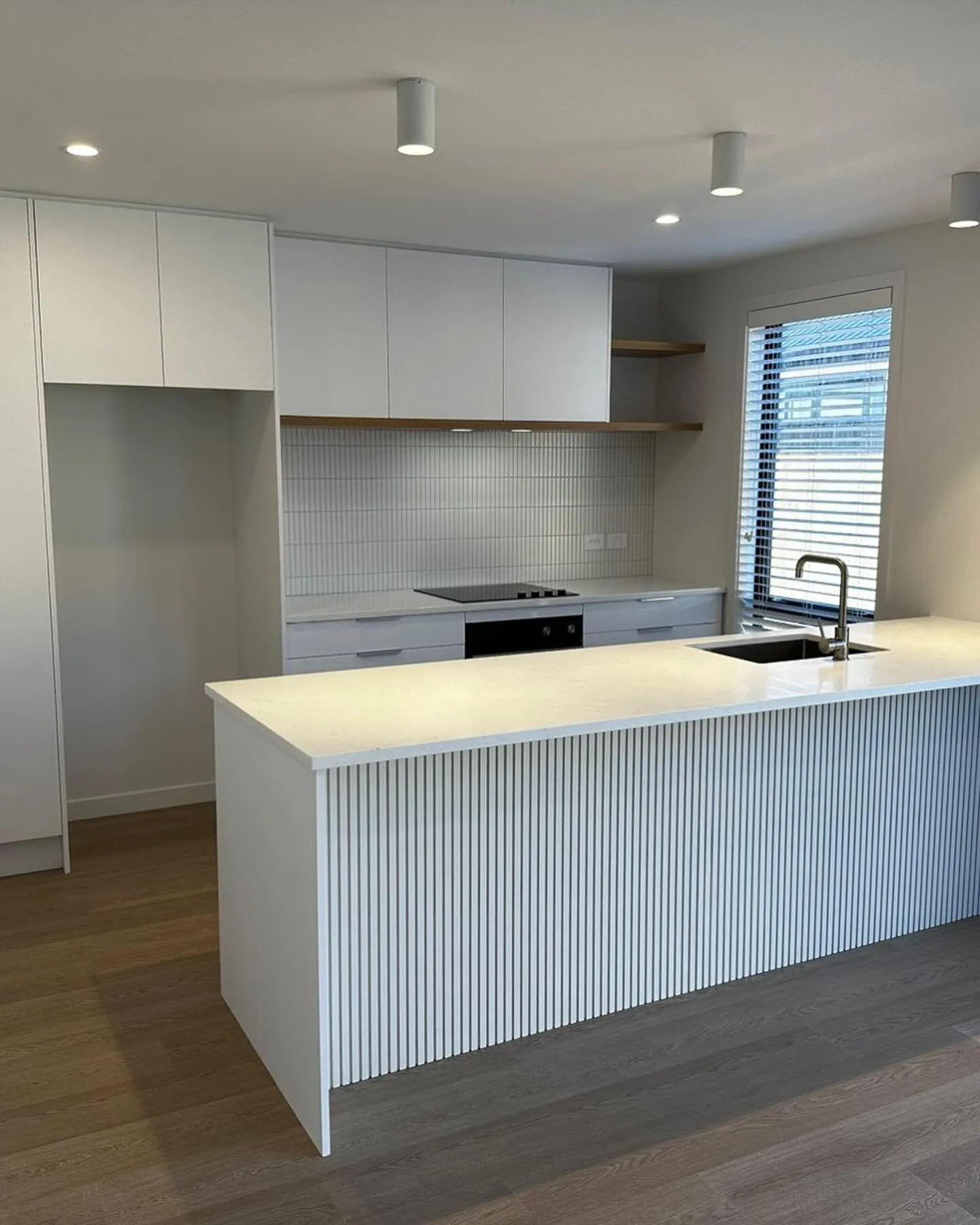 White kitchen with a fluted peninsula panel, tiled splashback and floating shelf