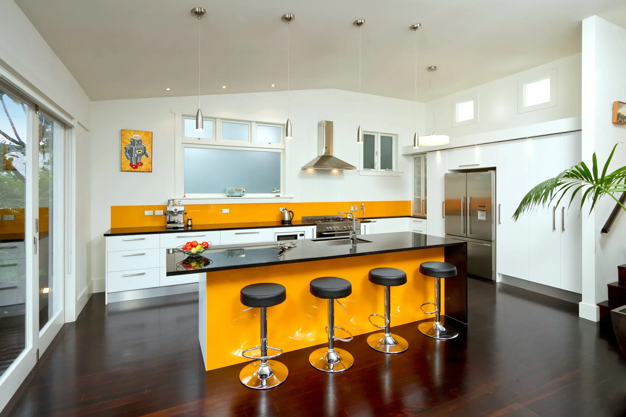 White kitchen with an orange glass splashback, matching island and bar stools