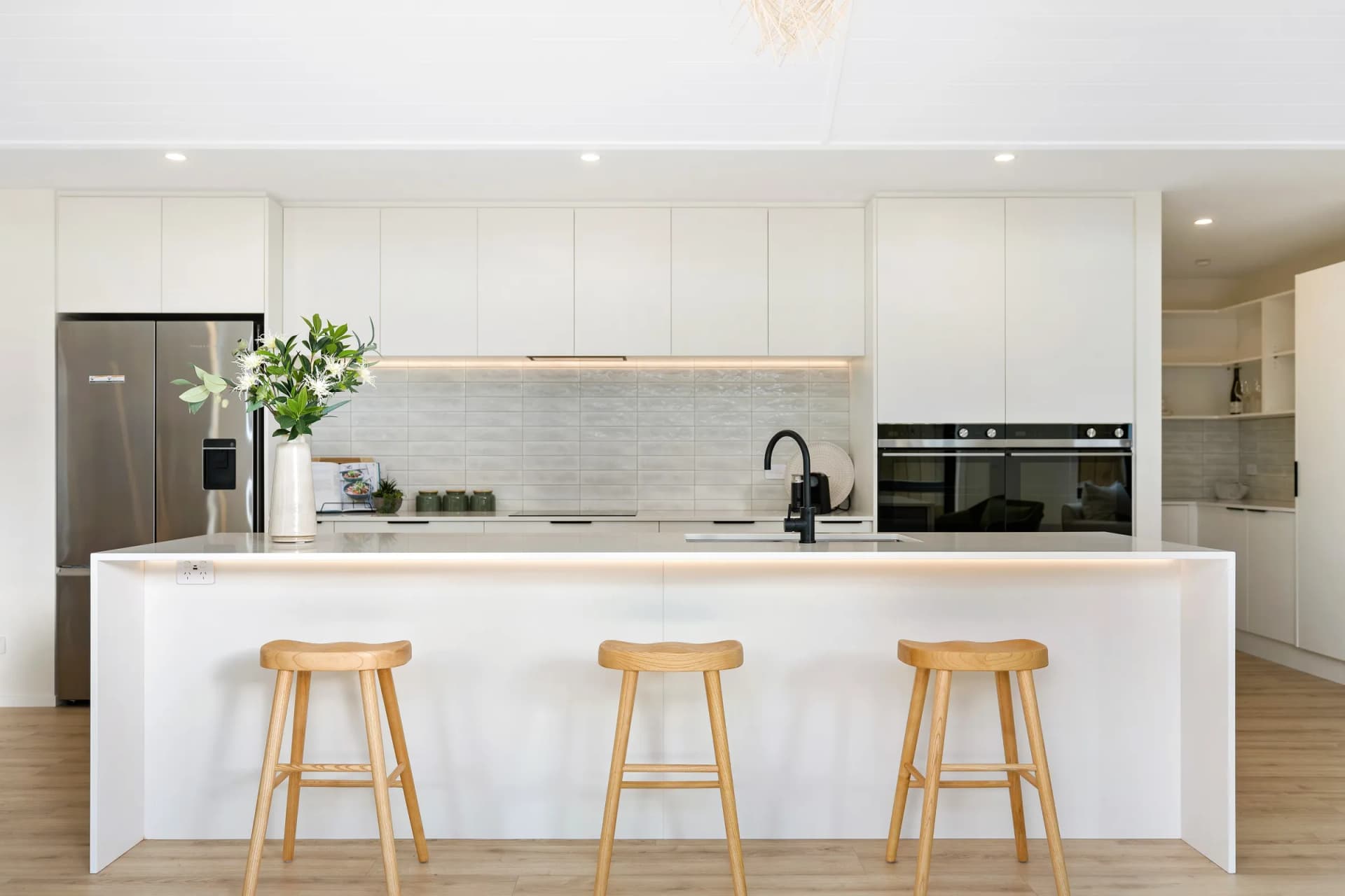 White kitchen with a long island, timber stools and a lit tiled splashback