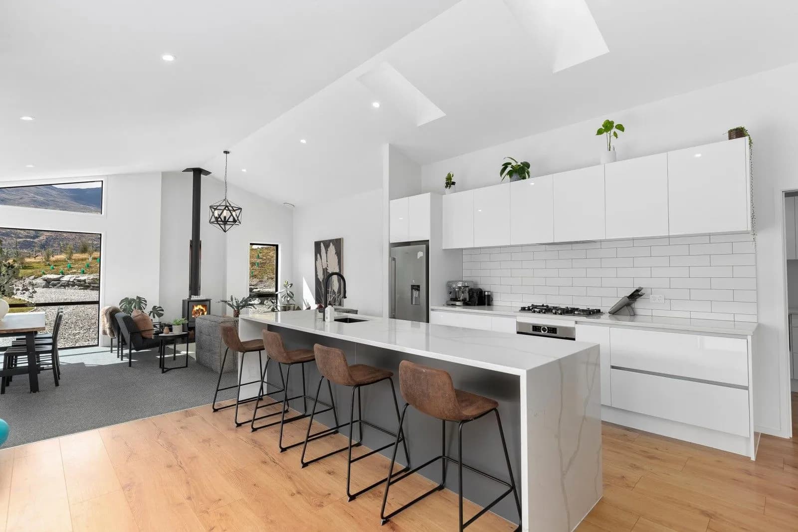 White kitchen with a stone-look waterfall island and bar stools under a skylight