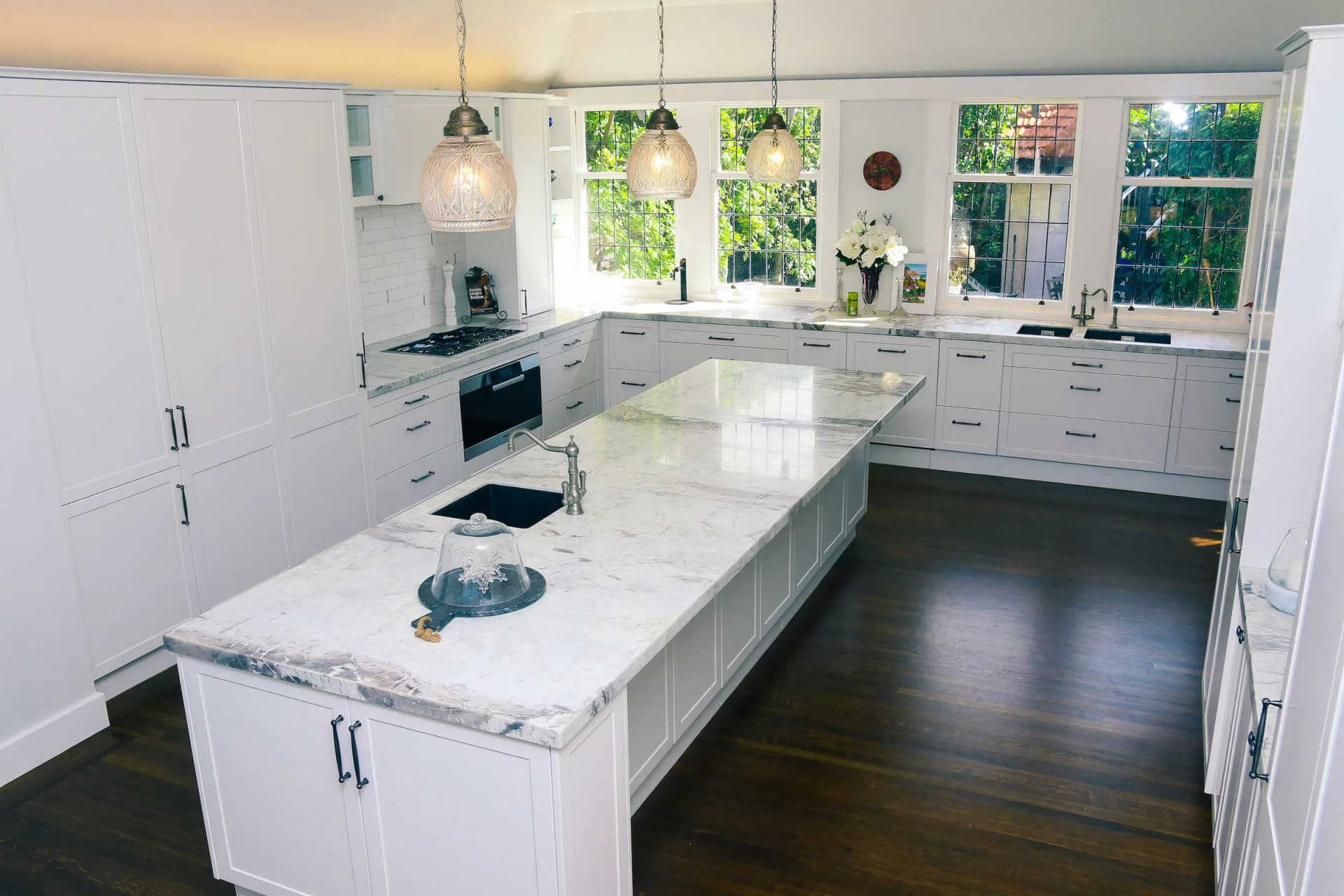 White shaker kitchen and long island with a marble-look benchtop below leadlight windows