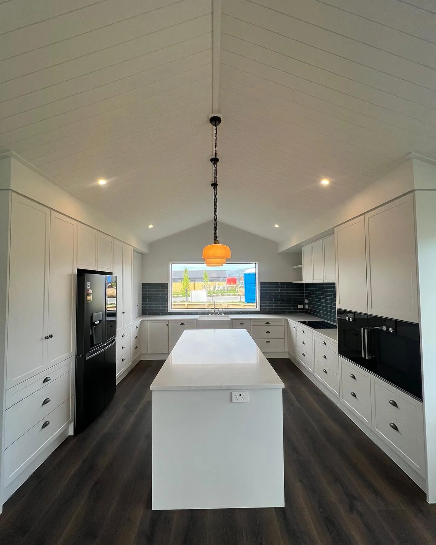 White shaker kitchen and island under a vaulted ceiling with a pendant light