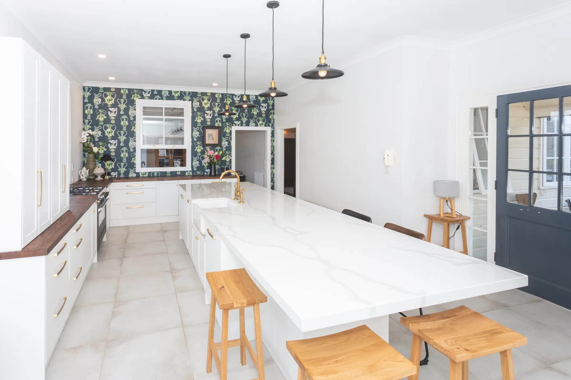 White shaker kitchen with a long marble-look island, timber stools and patterned wallpaper
