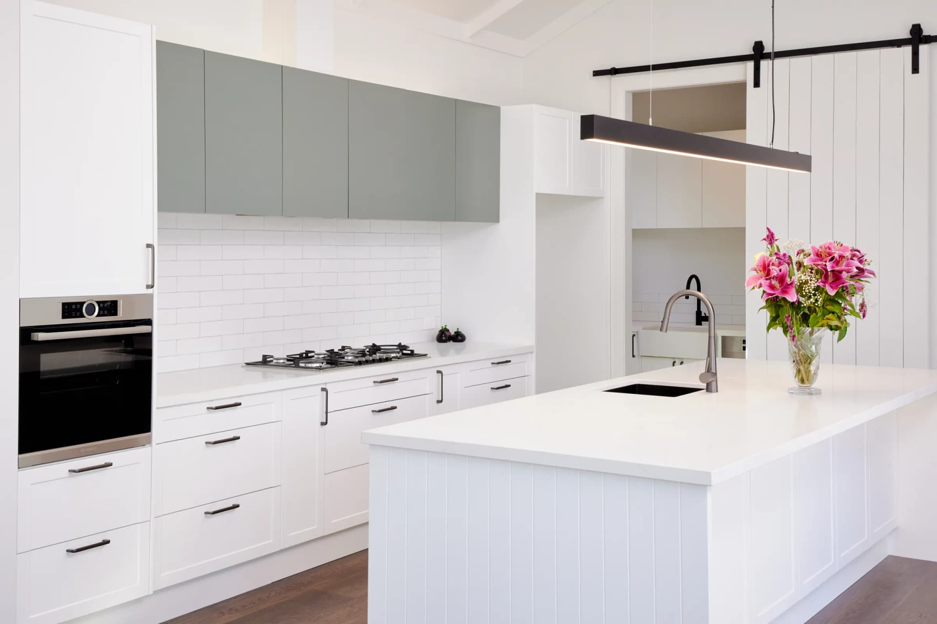Sage-green overheads above a white tiled splashback and white shaker drawers with black handles