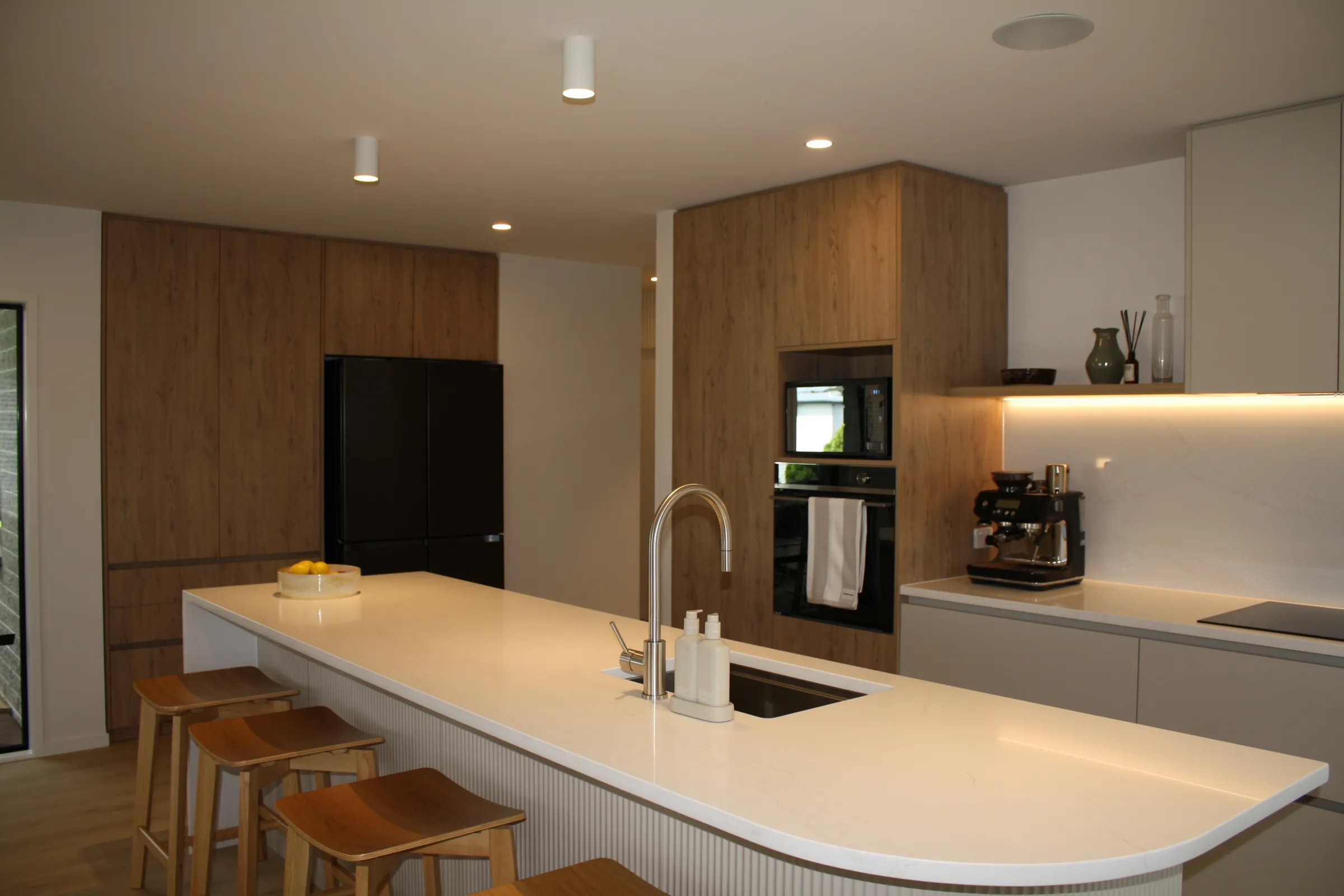 White island with a curved end and fluted panel in front of timber-look tall cabinets