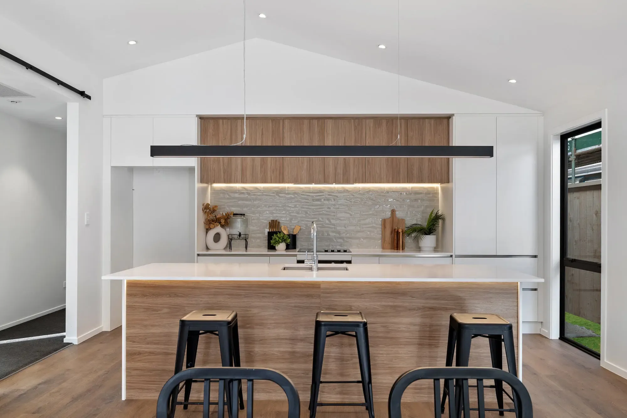 Timber-look island with stools in front of white cabinets and lit timber-look overheads