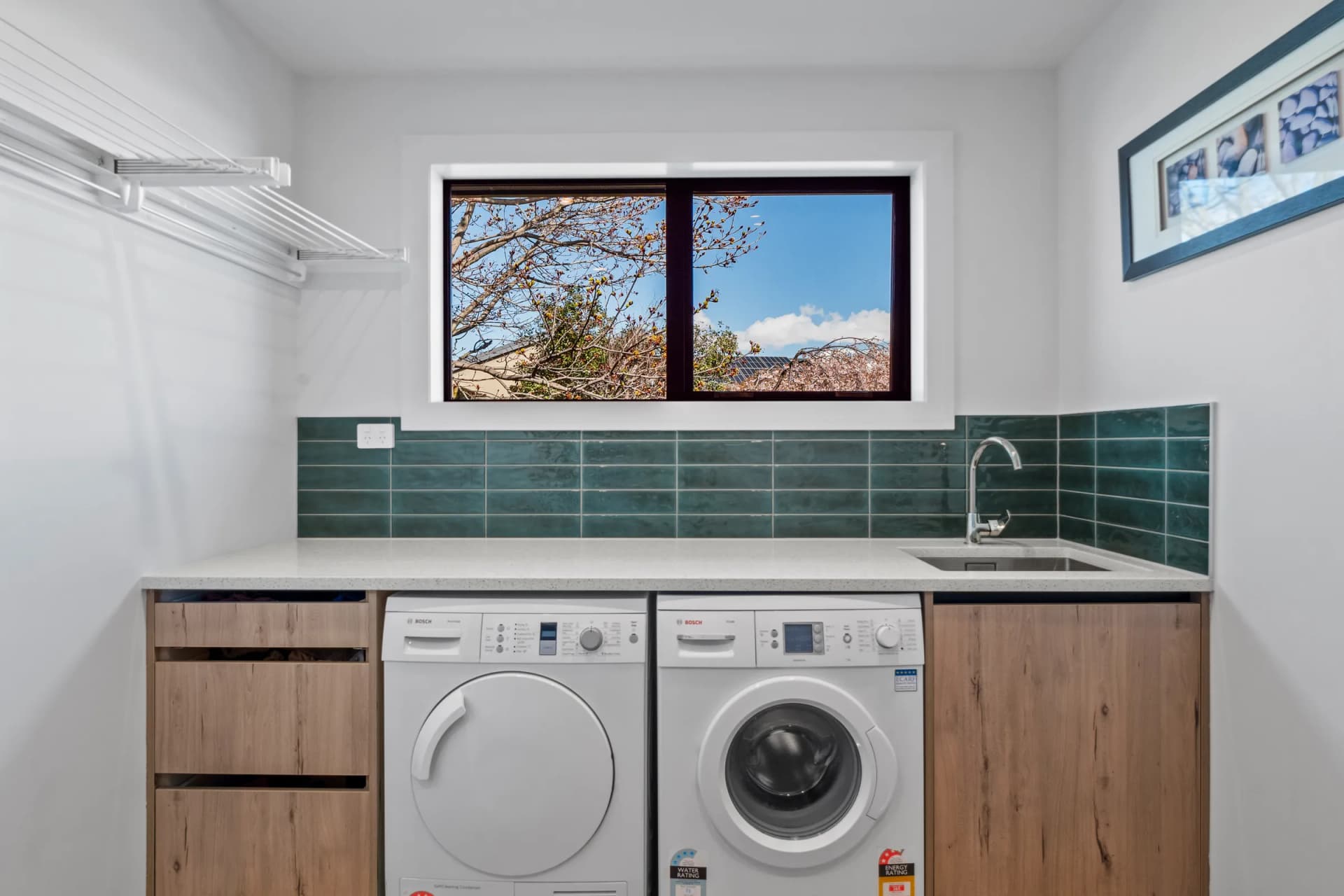 Timber-look laundry drawers either side of a washer and dryer with a green tiled splashback