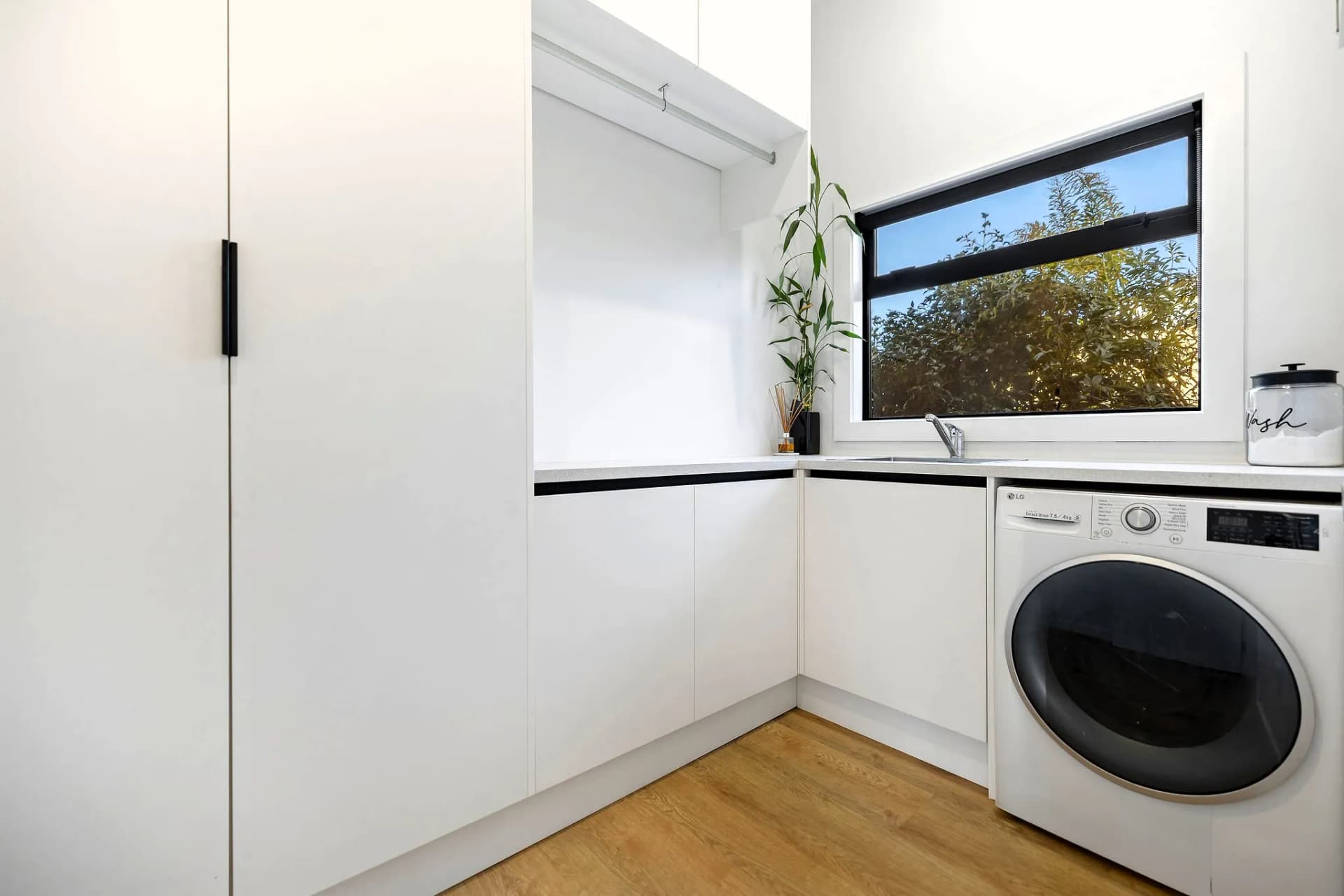 White L-shaped laundry with a front-loader and a tall cupboard
