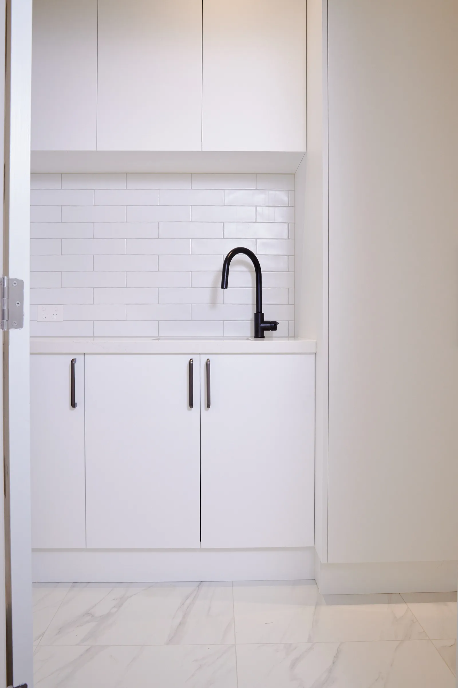 White laundry cupboards with black handles below a white subway tile splashback
