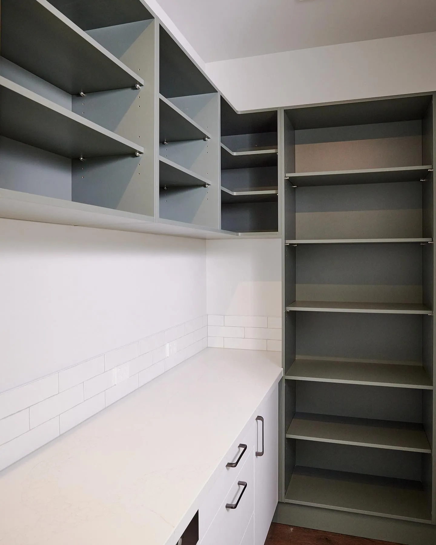 Walk-in pantry with grey open shelving above a white bench and drawers