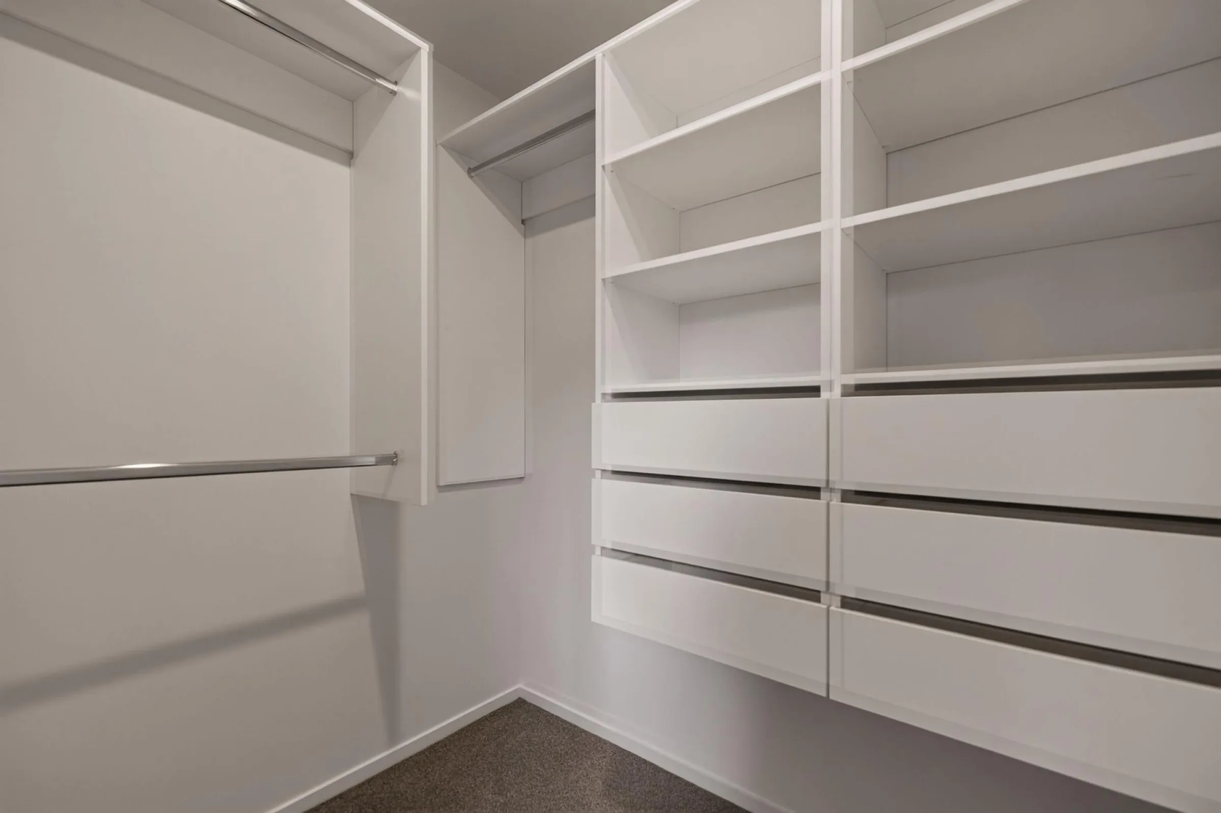White walk-in wardrobe with shelving, a drawer bank and a hanging rail