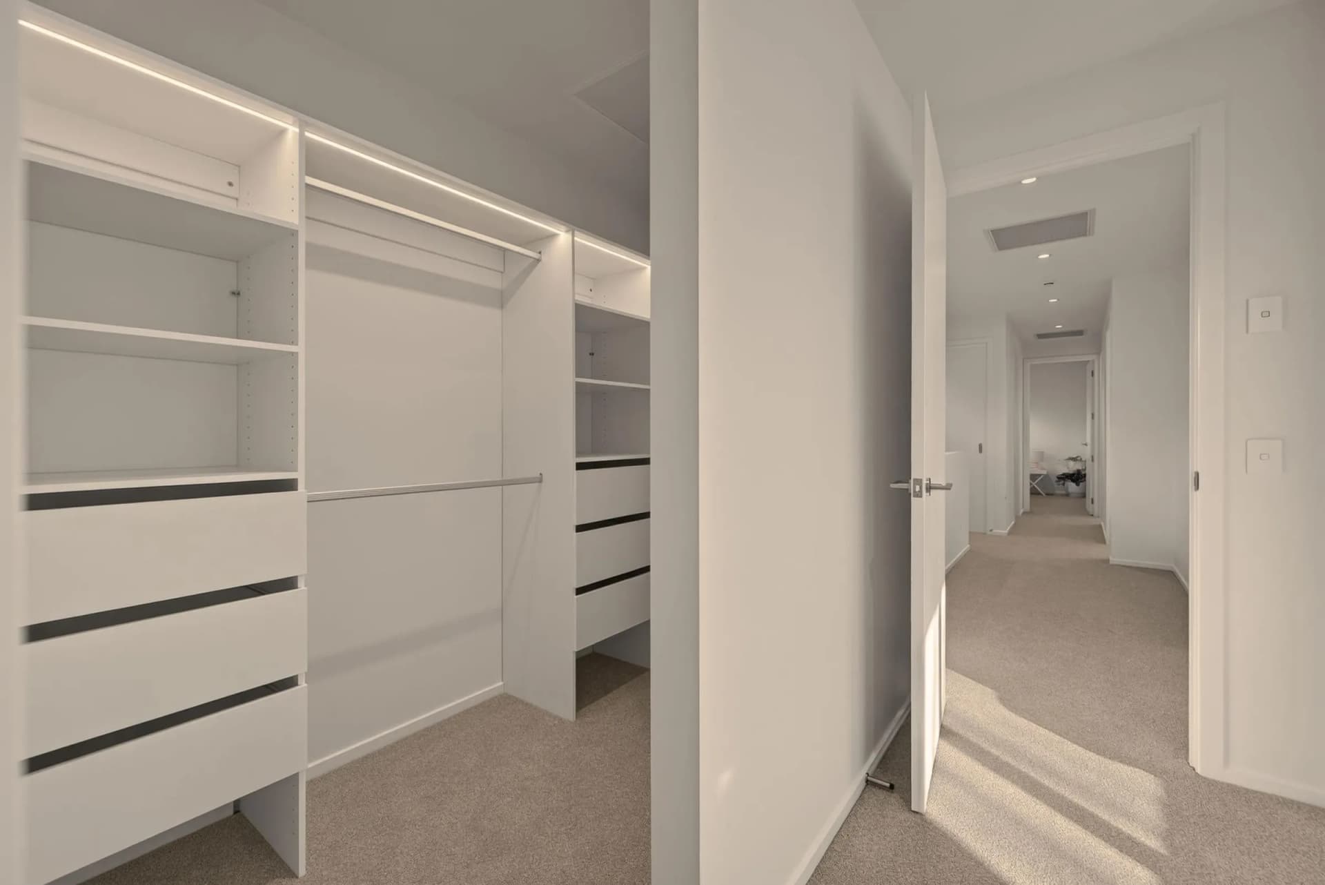 White walk-in wardrobe with a drawer bank, open shelving and LED strip lighting